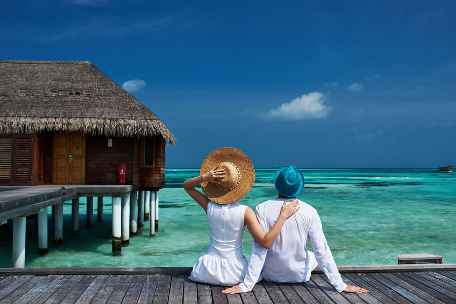 Couple on tropical beach luxury vacation by overwater bungalow