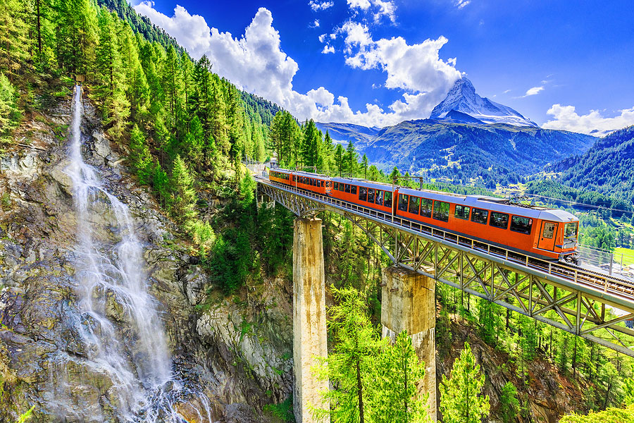 train on bridge near waterfall in switzerland